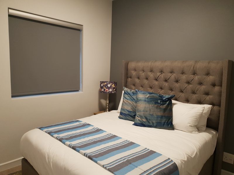 A well-maintained bedroom featuring a neutral color palette, an accent wall, and a fitted roller blind for privacy.