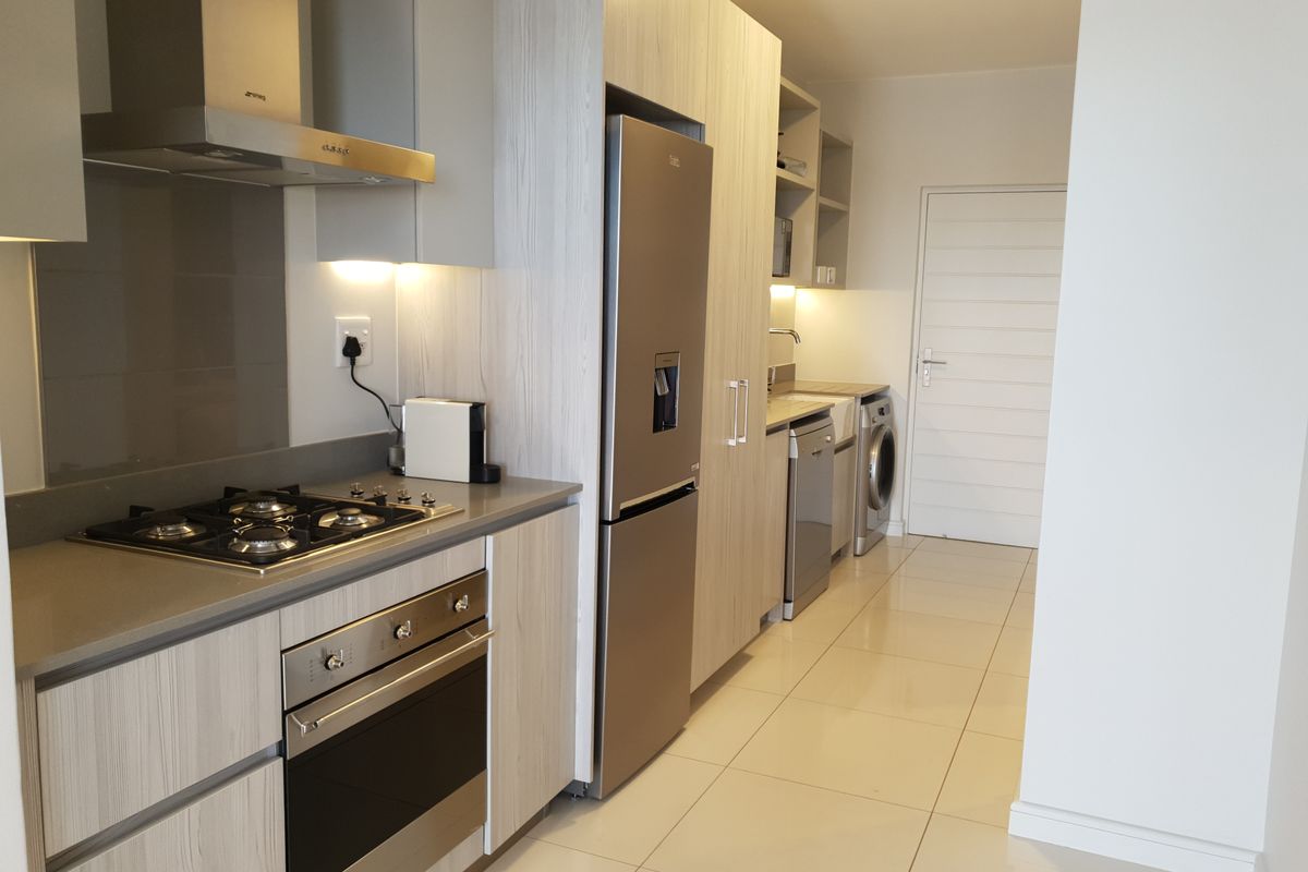 Modern kitchen featuring light wood-grain cabinetry, stone countertops, gas hob, built-in oven, stainless steel extractor, and integrated appliances with sleek tiled flooring.