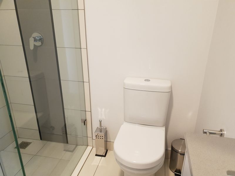 A clean and modern bathroom featuring a glass-enclosed shower and a white toilet with neutral tiled finishes.