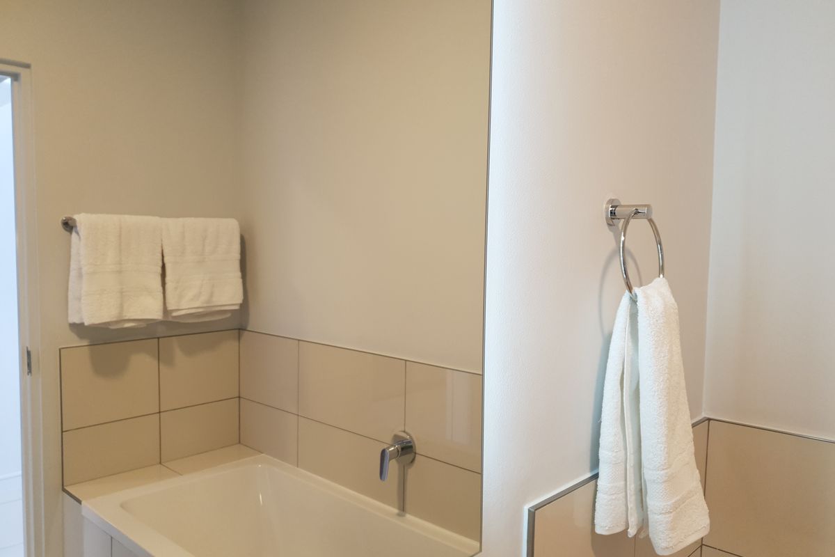 A clean and modern bathroom featuring a built-in bathtub with wall-mounted fixtures, neutral wall tiling, and a large vanity mirror.