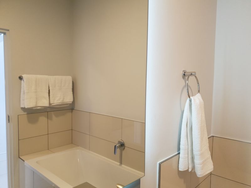 A clean and modern bathroom featuring a built-in bathtub with wall-mounted fixtures, neutral wall tiling, and a large vanity mirror.