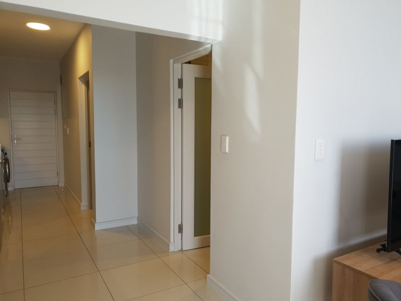 A clean, neutral hallway featuring tiled flooring and recessed lighting, providing access to multiple rooms within the apartment.
