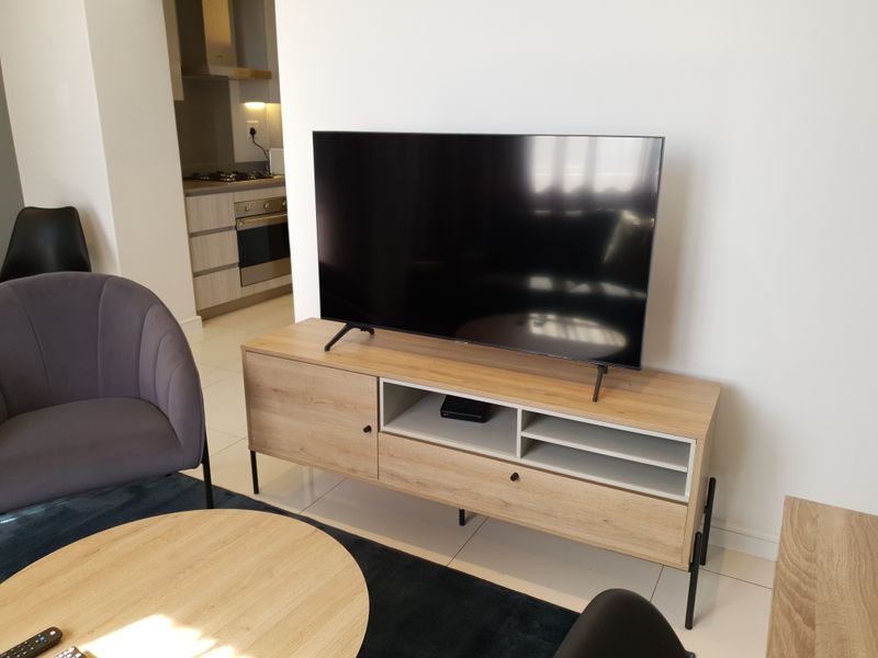 Open plan living area featuring modern kitchen cabinetry with integrated oven and hob, flowing into a comfortable lounge space with tiled flooring.