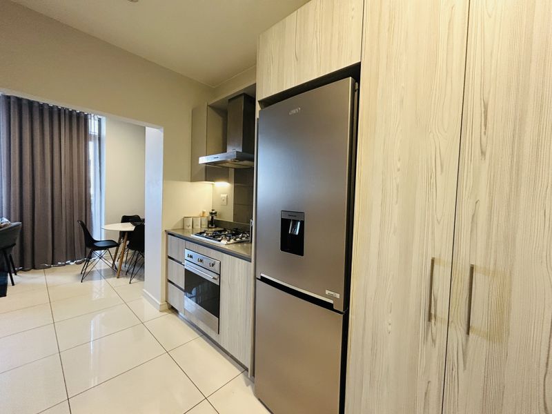 Modern kitchen featuring light wood-grain cabinetry, stainless steel built-in oven, gas hob, extractor fan, and tiled flooring, seamlessly connected to the adjacent dining area.