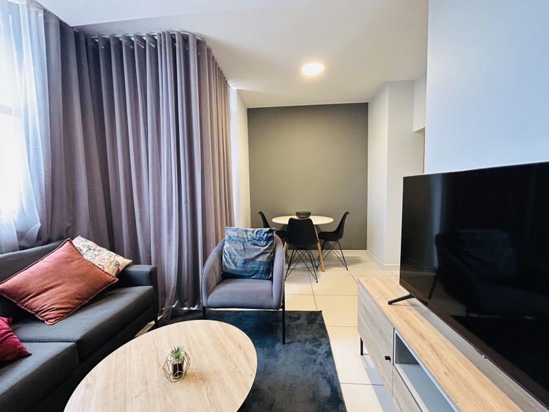 A well-maintained living area featuring neutral tiled flooring, recessed lighting, and floor-to-ceiling curtains, creating a comfortable and modern atmosphere.