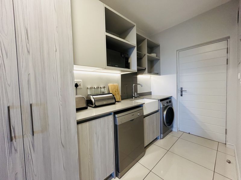 A modern, well-maintained scullery featuring built-in cabinetry, an under-counter sink, integrated dishwasher, and sleek tiled flooring with efficient under-cabinet lighting.