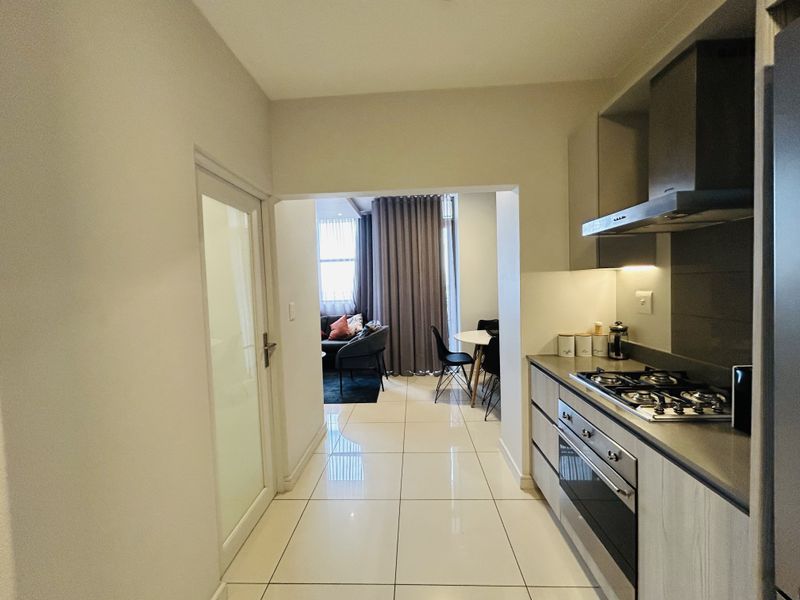 Modern open-plan kitchen featuring sleek cabinetry, integrated gas hob, and oven, flowing seamlessly into a bright living and dining area with tiled floors.