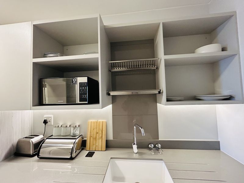 Modern kitchen area featuring sleek grey cabinetry, stone countertops, an undermount sink, and integrated microwave with under-cabinet lighting.