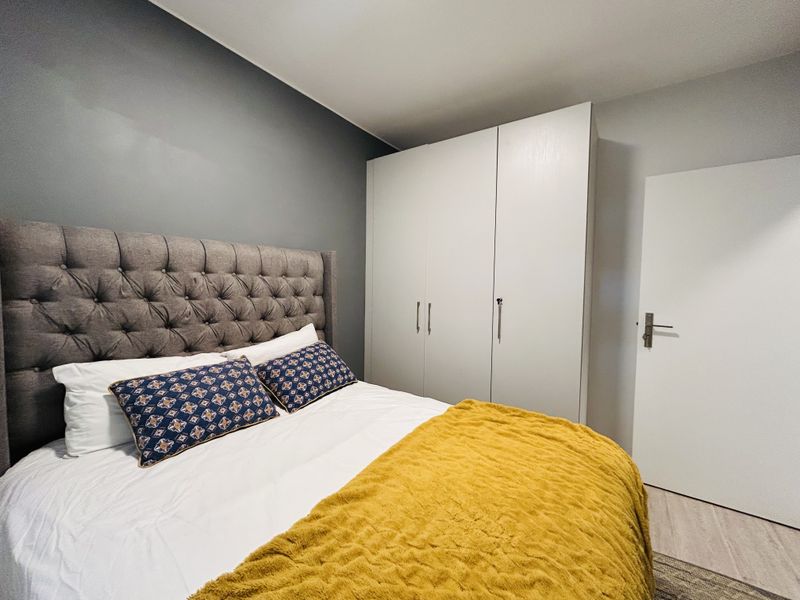 A well-maintained bedroom featuring a neutral color palette, a grey accent wall, and a large built-in wardrobe for storage.