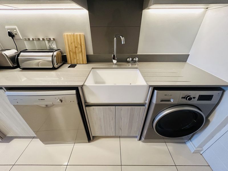 A modern, well-maintained laundry area featuring a farmhouse sink, stone countertops, and integrated cabinetry with clean tiled flooring.