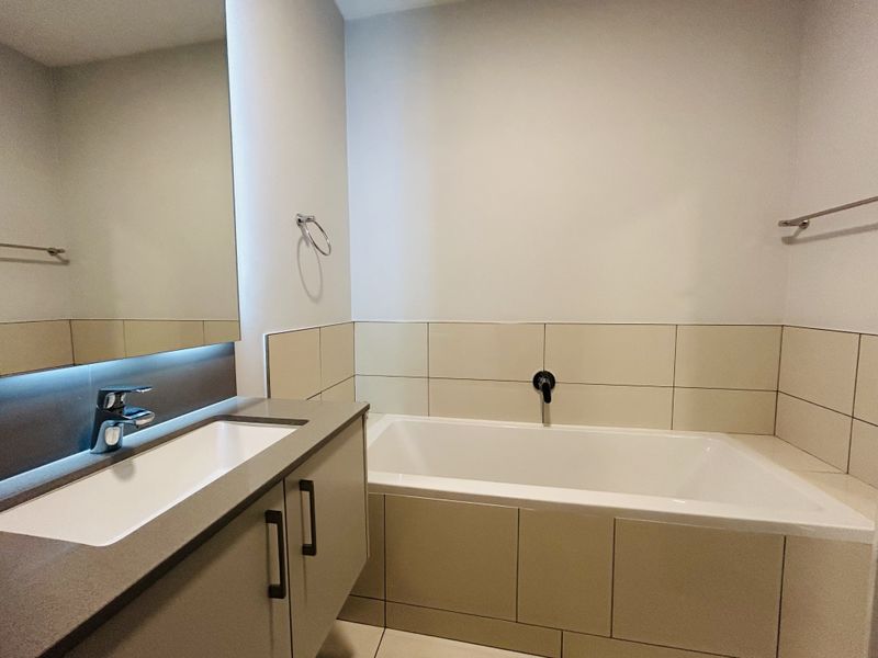A modern, well-maintained bathroom featuring a built-in vanity with integrated basin, large wall mirror, and a tiled bathtub surround.