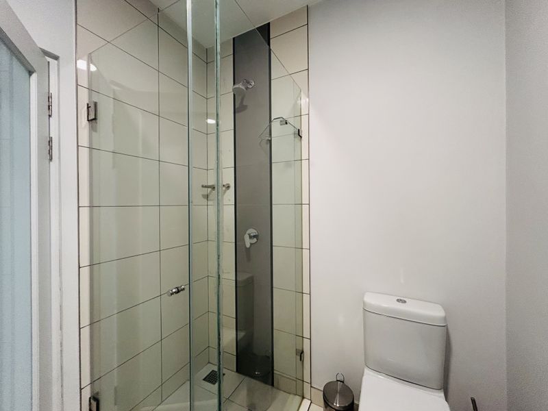 A clean and modern bathroom featuring a glass-enclosed shower with tiled walls and a standard white toilet.