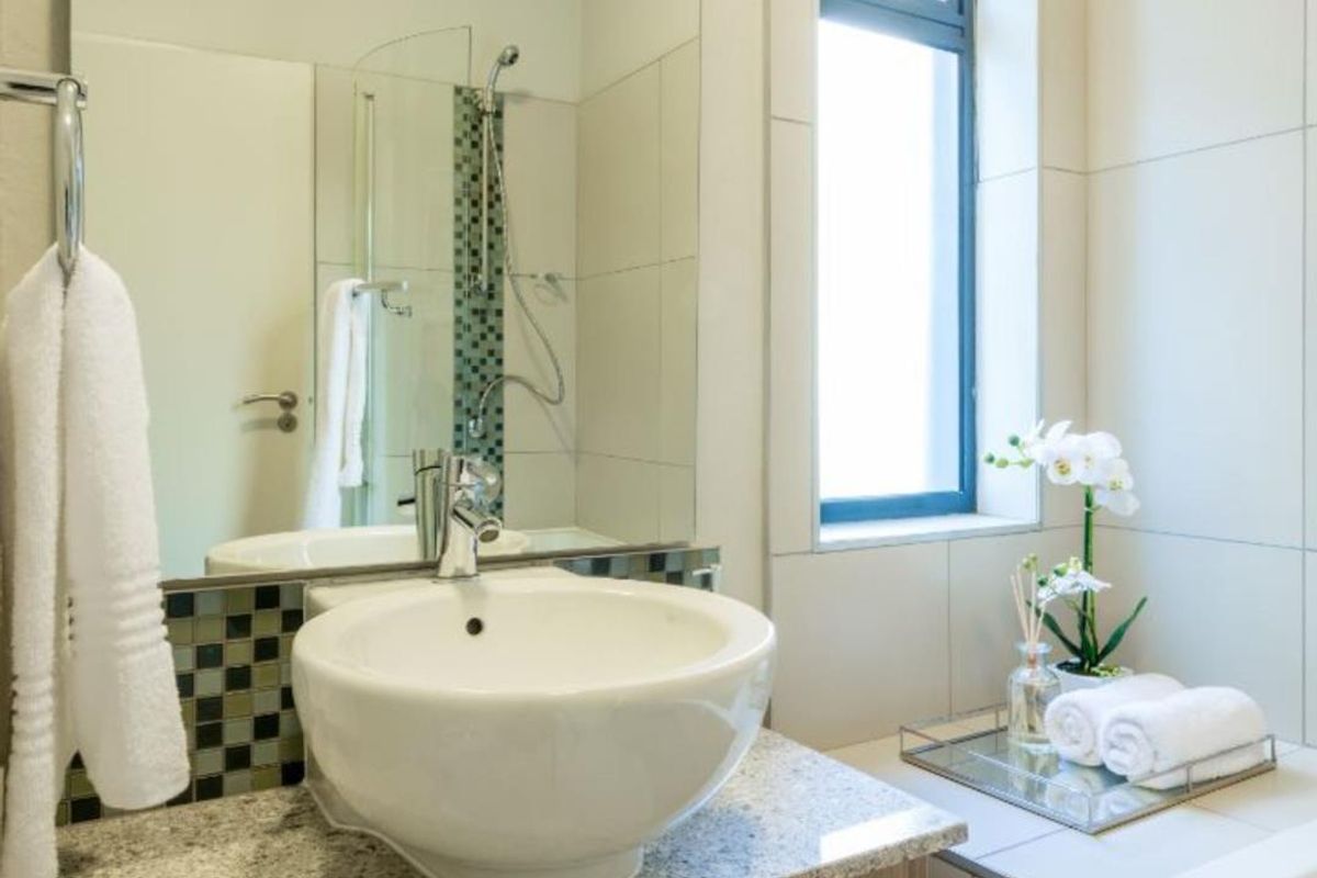 Modern bathroom featuring a vessel sink on a granite vanity, large wall mirror, mosaic tile accents, and a glass-enclosed shower area.