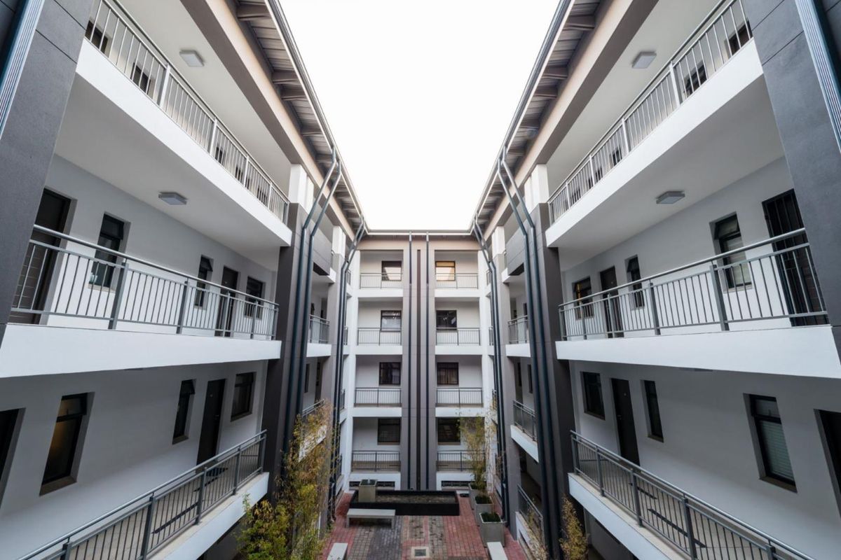 A modern apartment complex courtyard featuring multi-level balconies, metal railings, and a paved central area with architectural lighting.