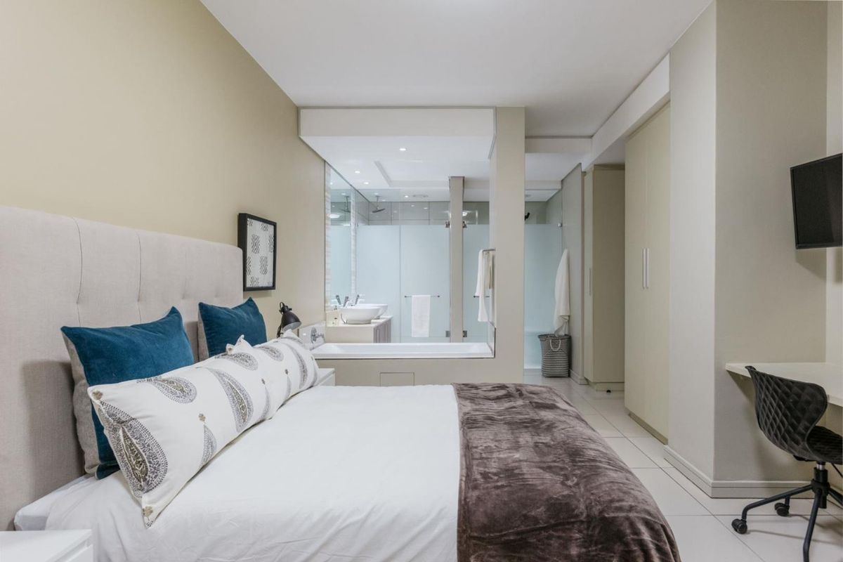Modern bedroom featuring an open-plan en-suite bathroom with a soaking tub, glass shower enclosure, and built-in cabinetry.