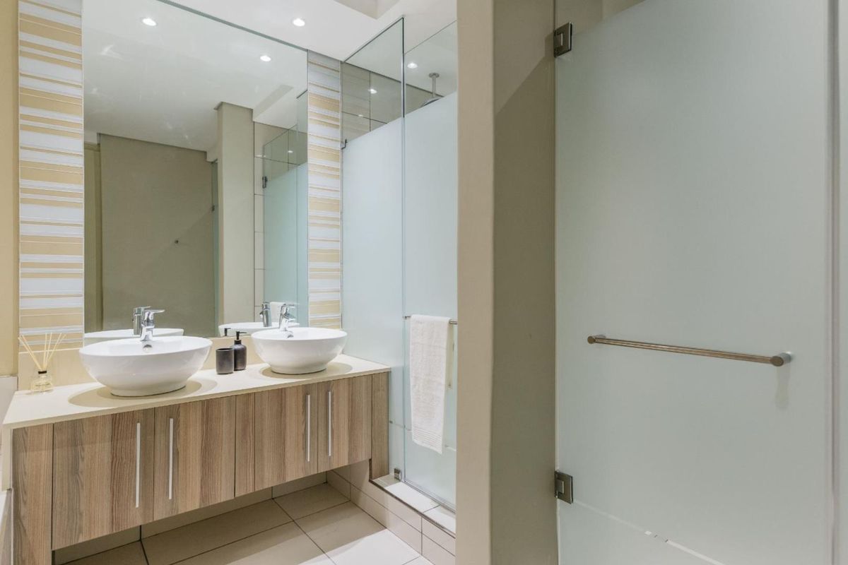 Modern bathroom featuring a floating double vanity with vessel sinks, large wall-mounted mirror, and a glass-enclosed shower with frosted privacy panels.