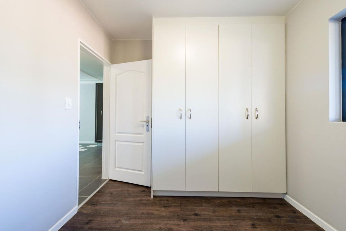 A bedroom featuring built-in white cabinetry and dark wood-look flooring, with a doorway leading to an adjacent tiled area.