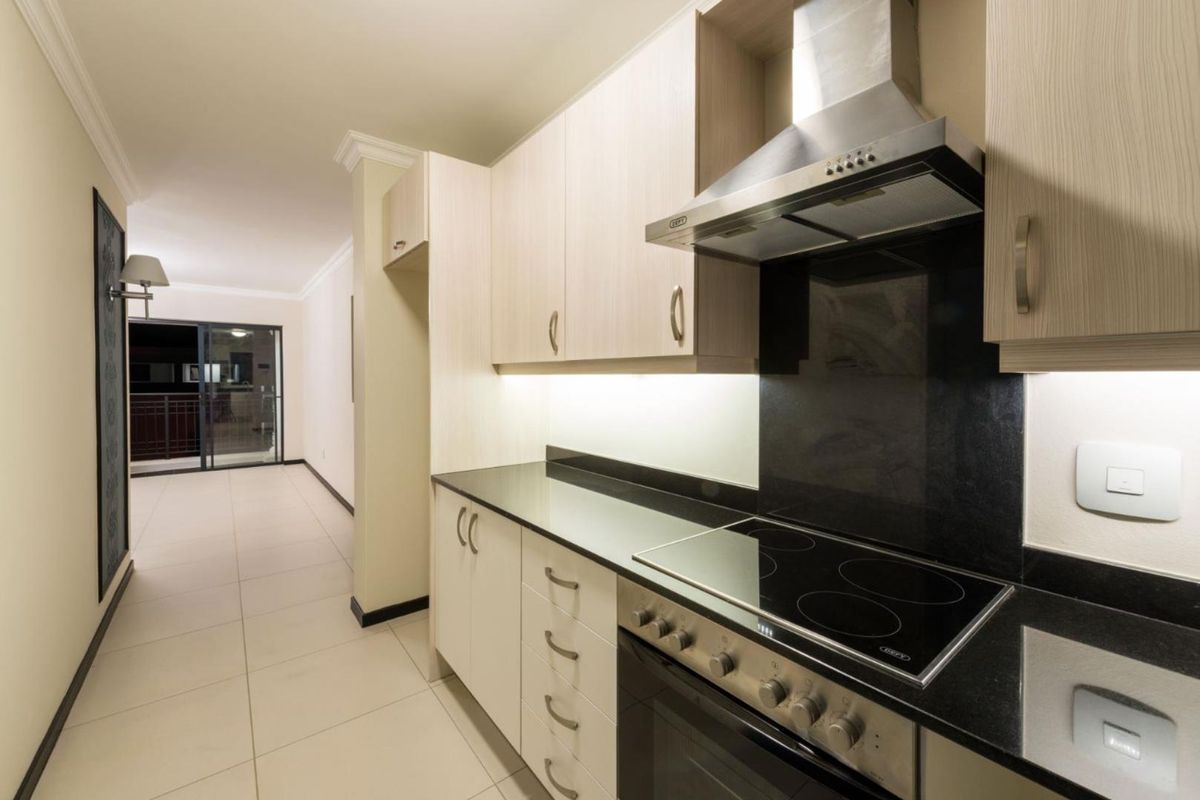 Modern kitchen featuring light wood cabinetry, black granite countertops, a built-in oven, and a stainless steel extractor fan, leading into an open-plan living area.