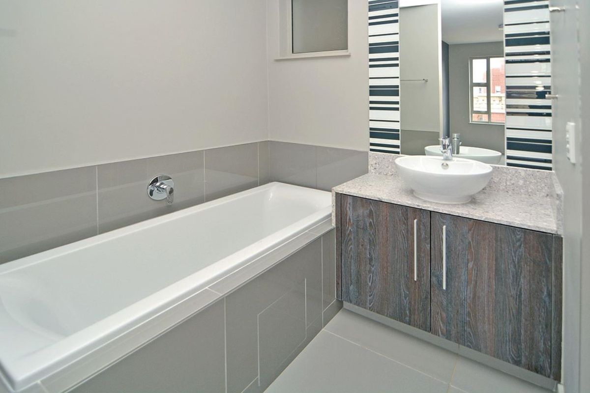 Modern bathroom featuring a built-in bathtub, vanity cabinet with countertop basin, and neutral grey tiling throughout.