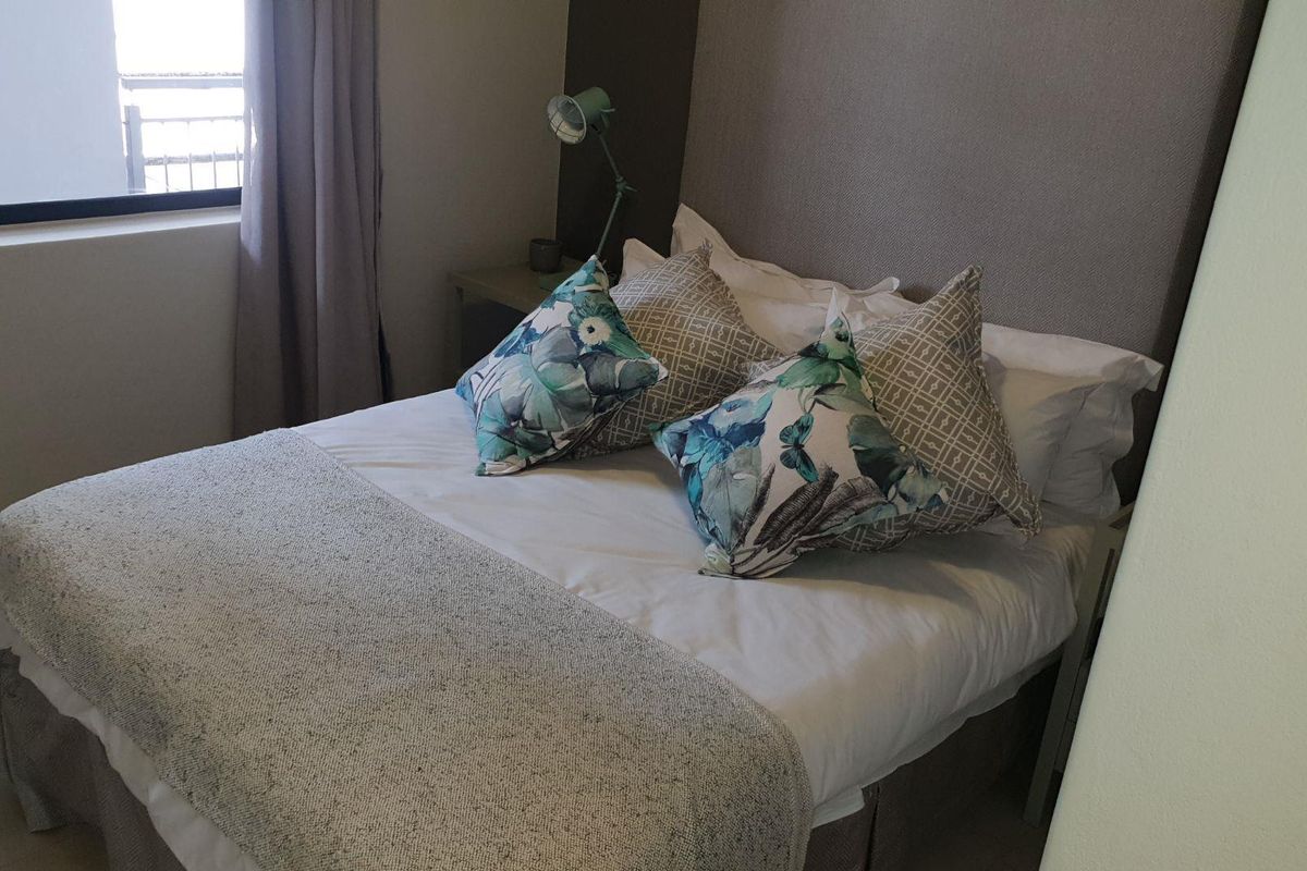 A well-maintained bedroom featuring a neutral upholstered headboard and natural light from the adjacent window.