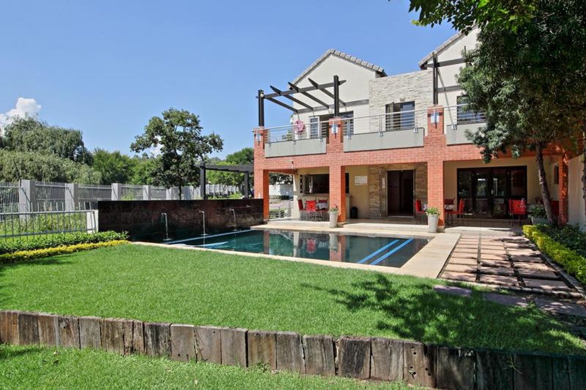 Rear exterior view featuring a swimming pool with a water feature, a paved patio area, and a balcony with a timber pergola.