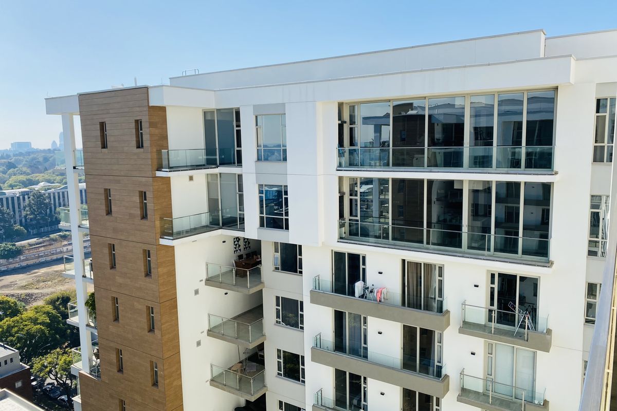 An elevated exterior view of a modern apartment building featuring multi-level balconies with glass balustrades and contemporary timber-look facade accents.