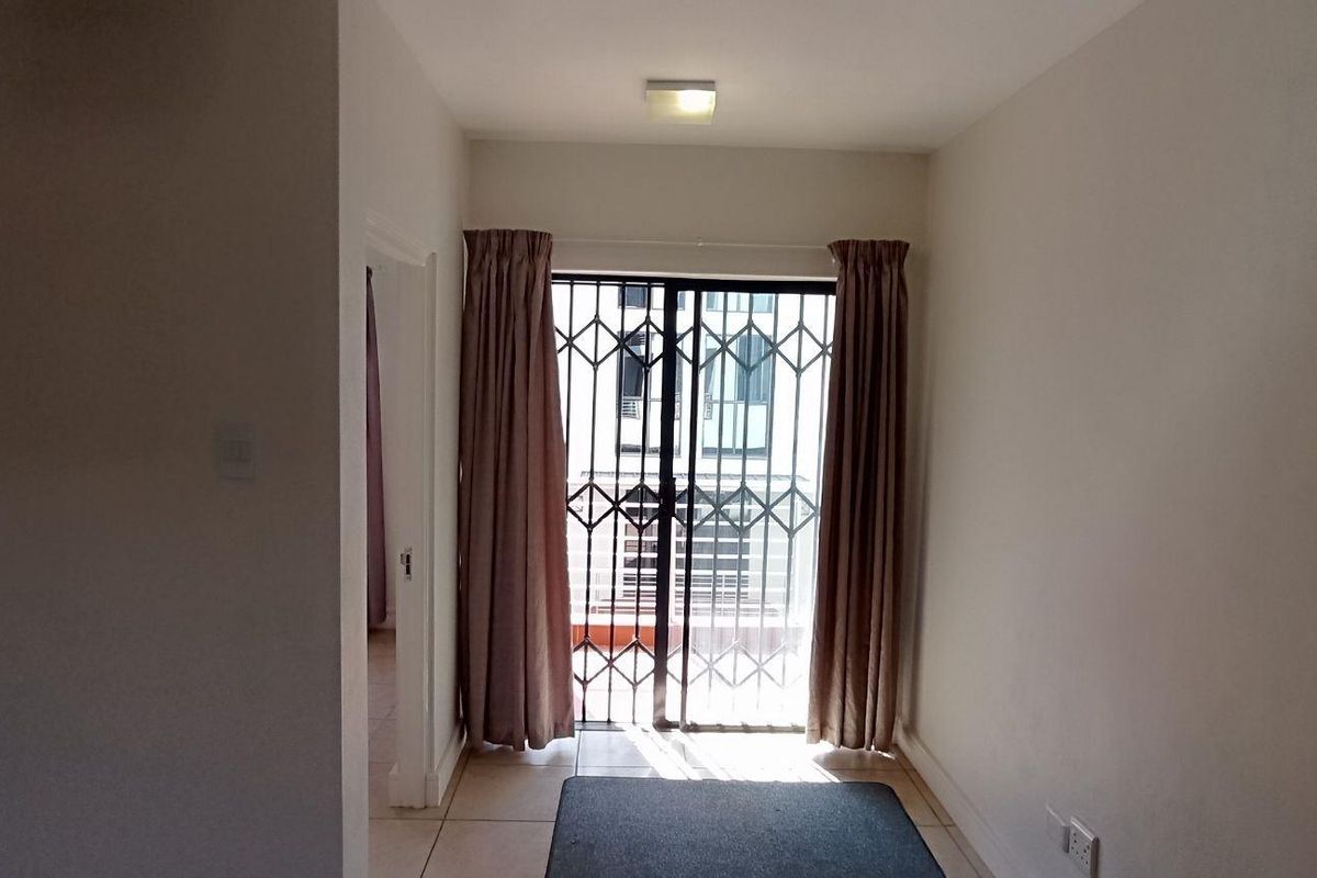 An empty living area featuring tiled flooring, a ceiling light, and a sliding door with a security gate leading to an outdoor space.