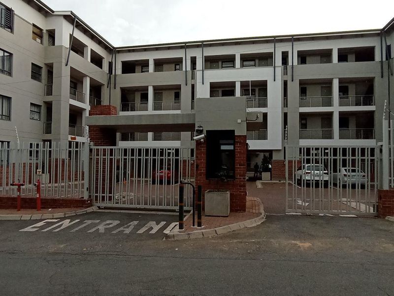 Front exterior view of a multi-story apartment complex featuring a secure gated entrance, brick perimeter wall, and electric fencing.