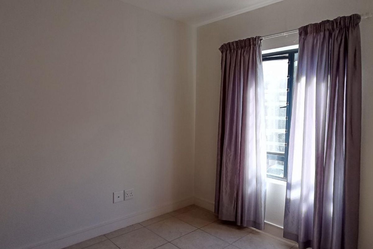 An empty bedroom featuring tiled flooring, a built-in cupboard, and natural light through a window with curtains.