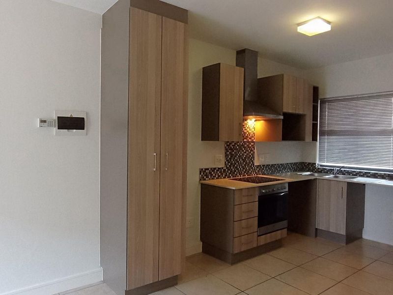 A modern, compact kitchen featuring built-in cabinetry, an electric oven with hob, extractor fan, and tiled flooring in an open-plan layout.