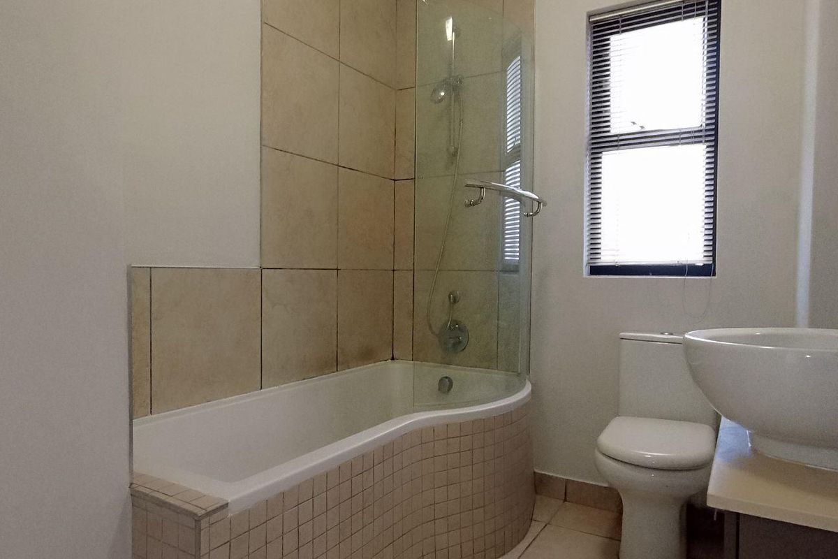A functional bathroom featuring a curved bathtub with a glass screen, a vessel sink vanity, and a toilet, offering a clean and practical layout.