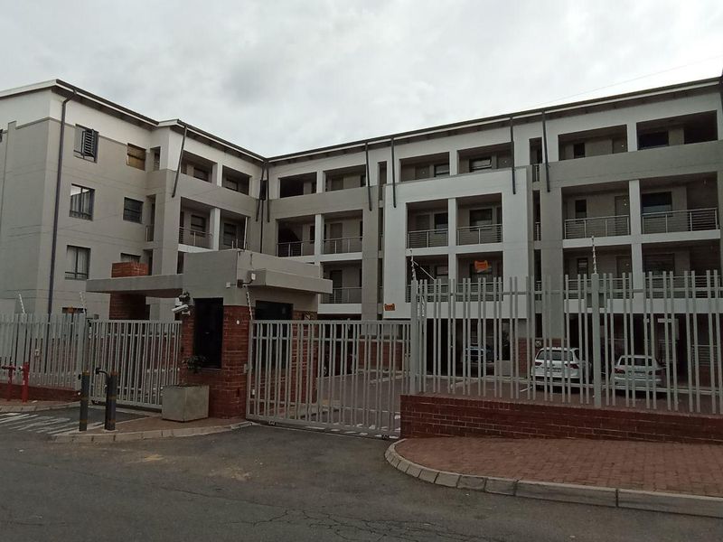 Exterior view of the apartment complex entrance featuring a secure gated access point, brick boundary walls, and electric fencing.