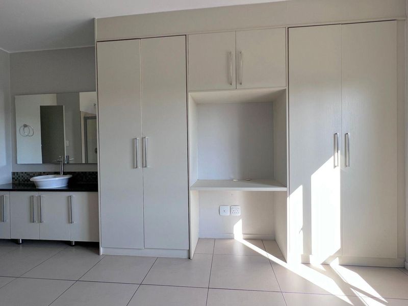 Spacious bedroom featuring extensive built-in cabinetry, a dedicated desk area, and a convenient integrated vanity with a modern vessel sink.
