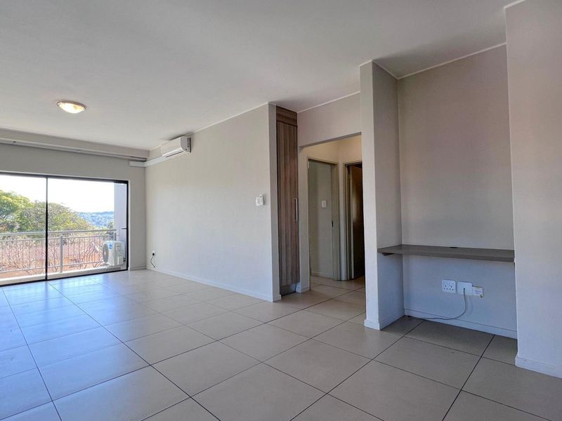 Spacious, light-filled living area featuring neutral tiled flooring, a built-in desk, air conditioning, and direct access to a private balcony.