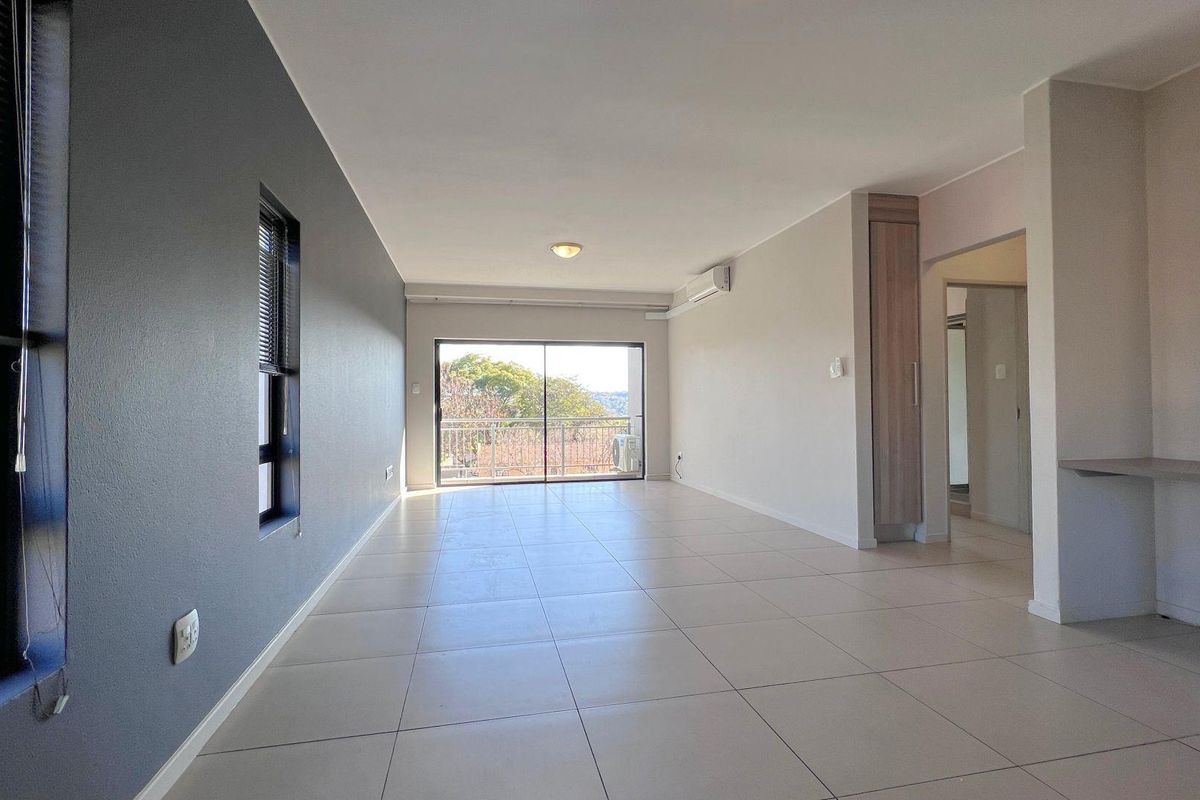 Spacious, light-filled living area featuring neutral tiled flooring, a built-in desk, integrated cabinetry, and sliding glass doors leading to an outdoor balcony.