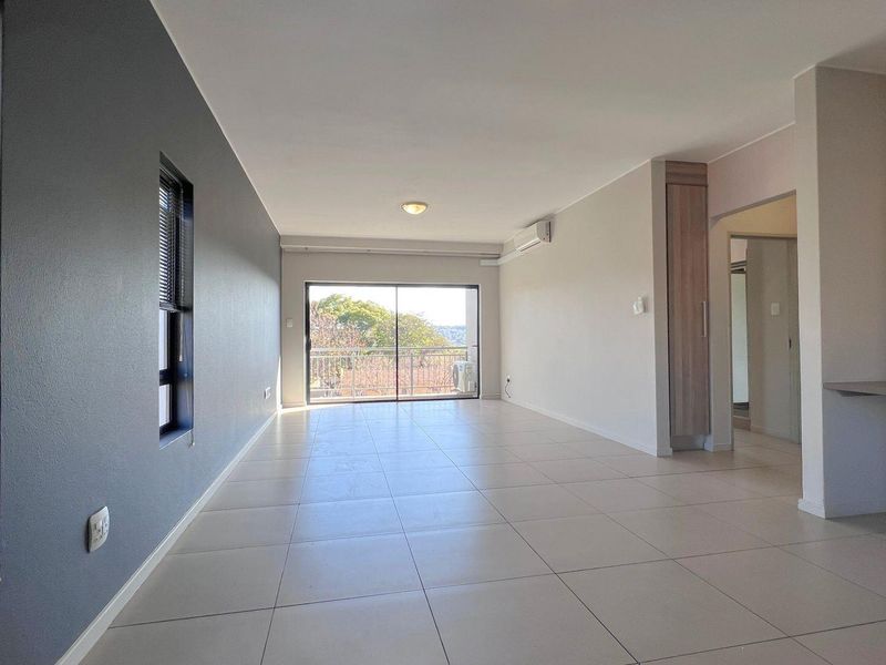 Spacious, light-filled living area featuring neutral tiled flooring, a built-in desk, integrated cabinetry, and sliding glass doors leading to an outdoor balcony.
