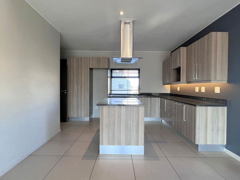 Modern kitchen featuring a central island, sleek laminate cabinetry, stone countertops, integrated extractor fan, and under-cabinet lighting with neutral tiled flooring.