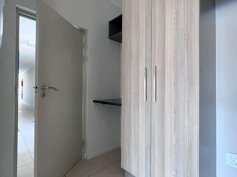 A clean, modern bedroom featuring built-in wood-grain wardrobes, integrated shelving, and neutral tiled flooring, offering a functional and well-maintained storage space.
