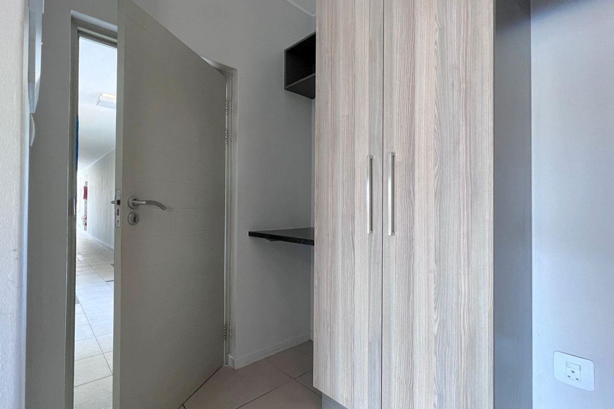 A clean, modern bedroom featuring built-in wood-grain wardrobes, integrated shelving, and neutral tiled flooring, offering a functional and well-maintained storage space.