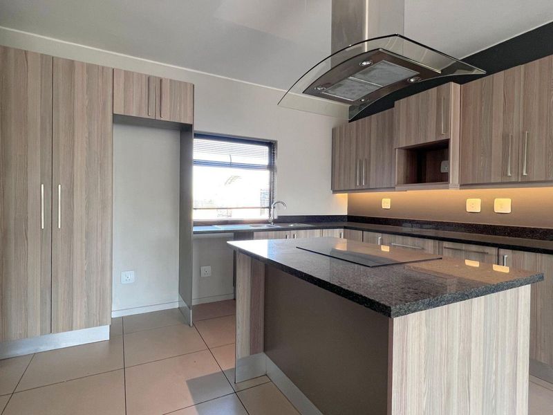 Modern kitchen featuring light wood-grain cabinetry, dark granite countertops, integrated hob, extractor fan, and under-cabinet lighting in an open-plan layout.