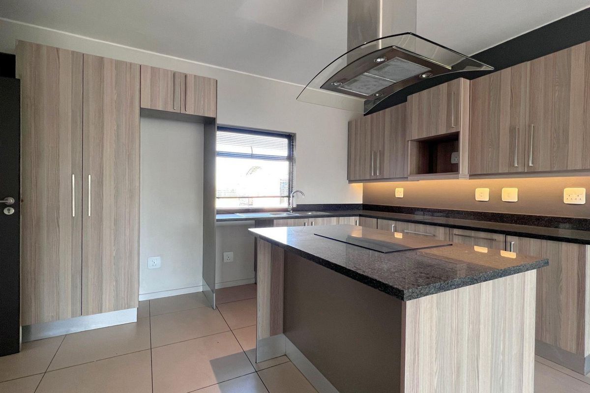 Modern kitchen featuring light wood-grain cabinetry, dark granite countertops, integrated hob, extractor fan, and under-cabinet lighting in an open-plan layout.
