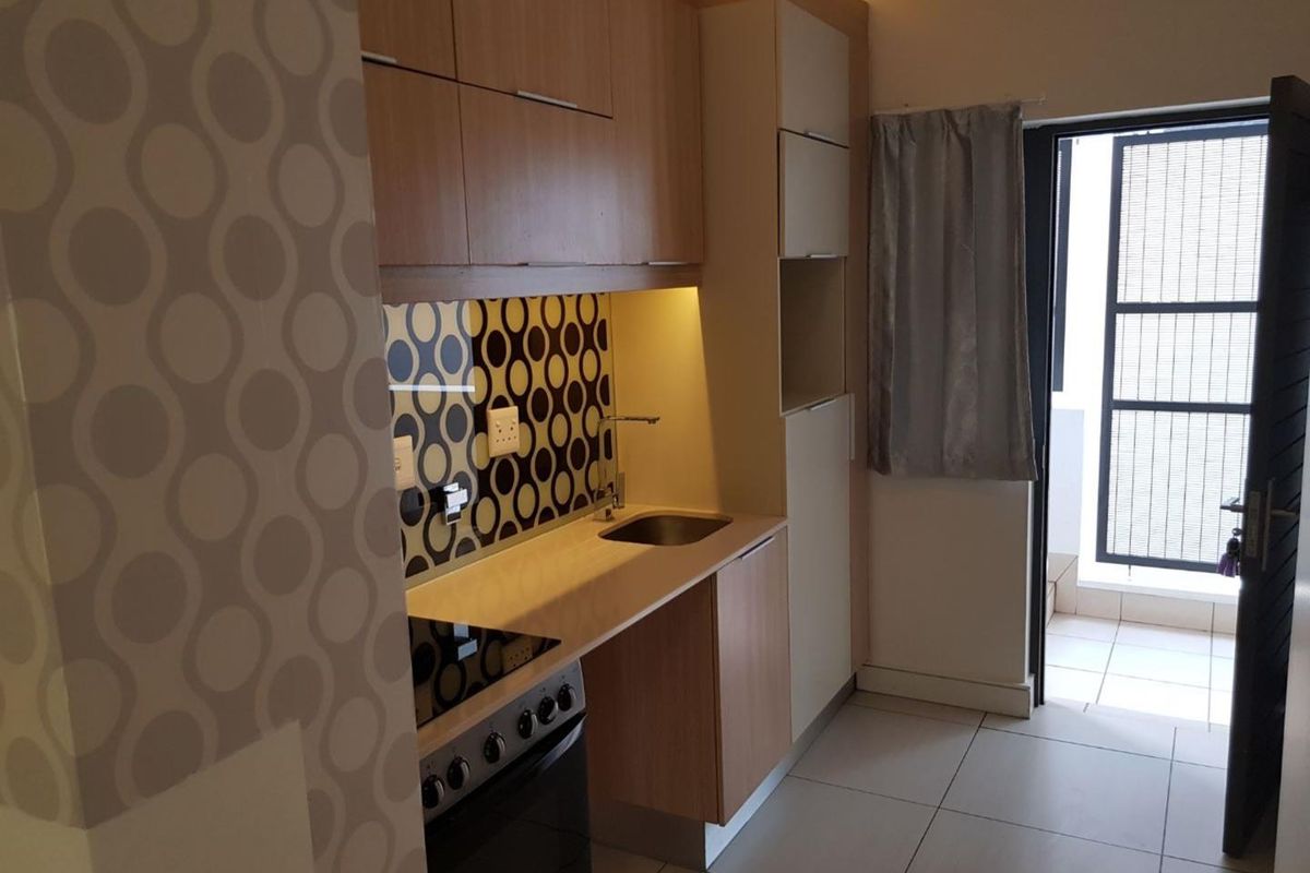 Compact kitchen featuring modern light wood cabinetry, a built-in electric stove, patterned tiled backsplash, and direct access to an outdoor balcony area.