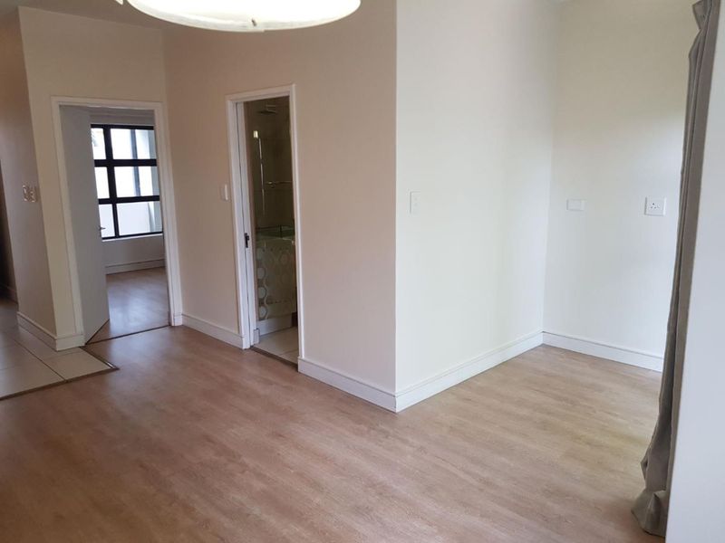 An empty living area featuring light-toned laminate flooring, neutral walls, and access to adjacent rooms including a bathroom.