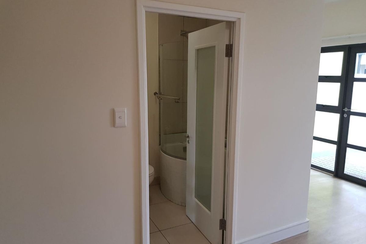 A view into a clean, compact bathroom featuring a shower enclosure, toilet, and tiled flooring, accessed via a modern frosted glass door.