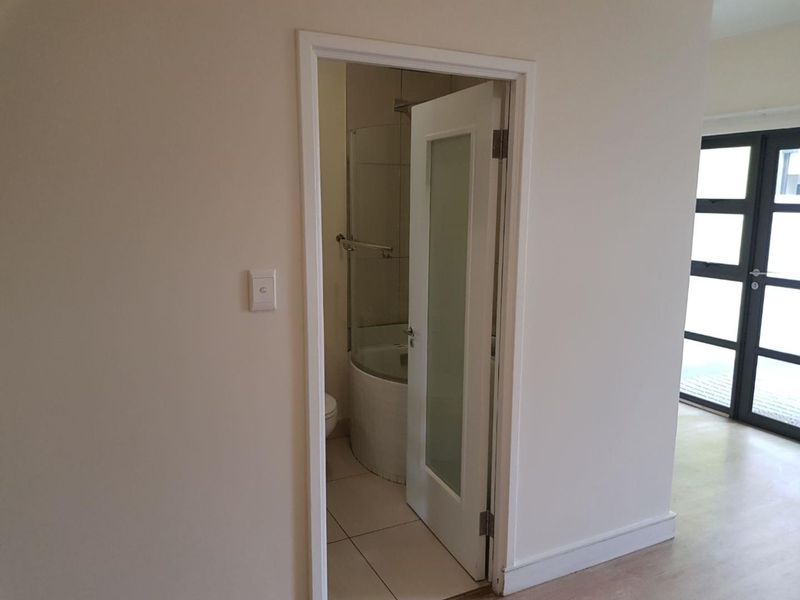 A view into a clean, compact bathroom featuring a shower enclosure, toilet, and tiled flooring, accessed via a modern frosted glass door.