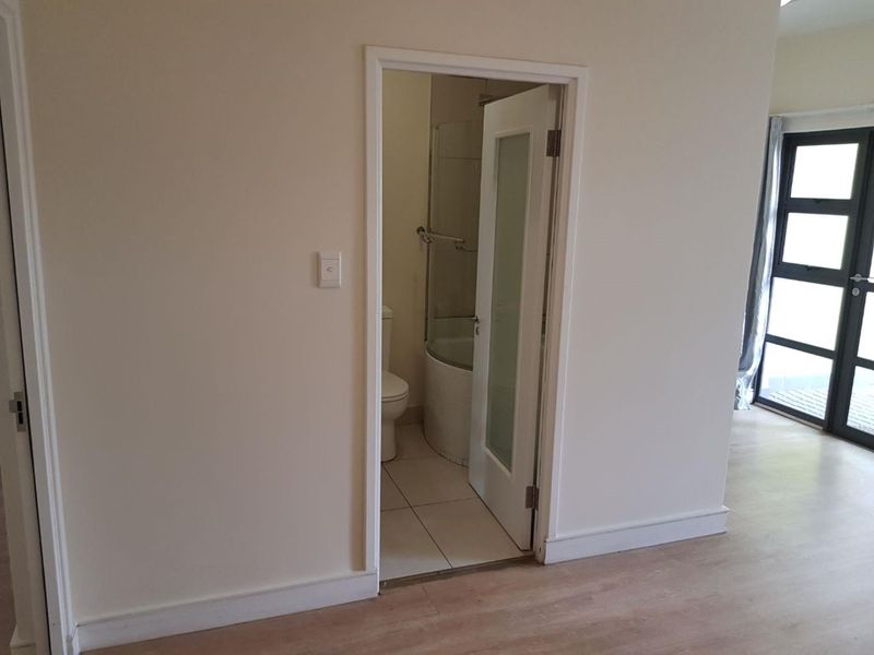 A view from a hallway looking into a bathroom, featuring neutral wall finishes, laminate flooring, and a glass-paneled door.
