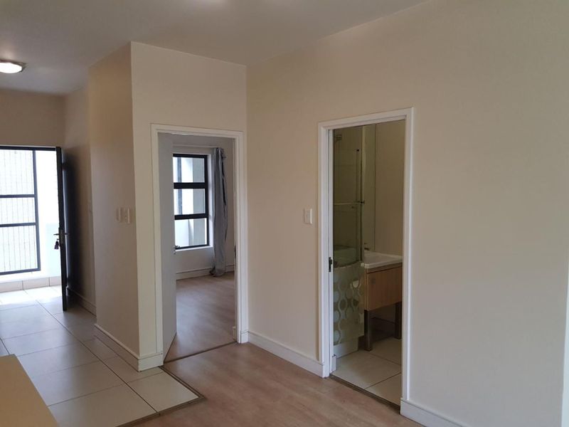A clean, neutral hallway connecting to a bedroom and bathroom, featuring a mix of tiled and laminate flooring with simple, modern finishes.