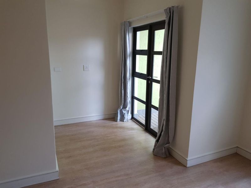 A bright, empty living area featuring modern laminate flooring and a double glass door providing access to the exterior.