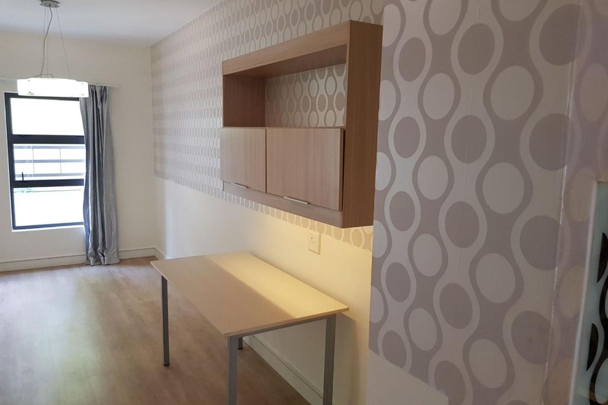 A bright bedroom featuring laminate flooring, patterned wallpaper, and built-in wall shelving, offering a clean and functional space.