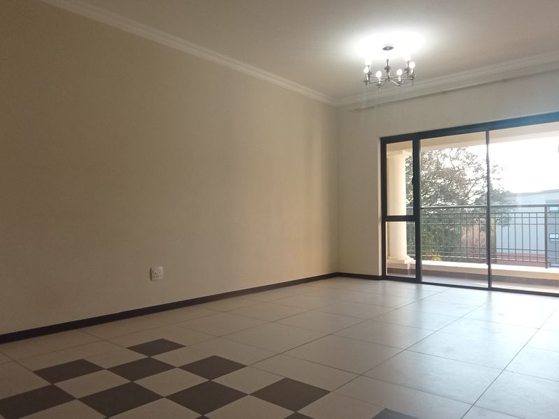 Spacious, empty living area featuring neutral tiled flooring, a built-in cupboard, and large sliding glass doors leading to an outdoor balcony.